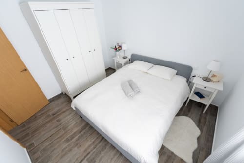 Dormitorio moderno en Smart Rent Fuerteventura con cama queen, cabecero gris, ropa de cama blanca y decoración minimalista cerca de Canarias