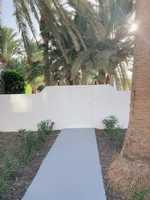 Puerta blanca y camino que conducen al apartamento Smart Rent Fuerteventura, rodeado de palmeras y paisajismo desértico