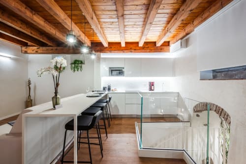 Cucina moderna con travi in legno a vista, mobili bianchi, isola con sedute e ringhiera in vetro nell'hotel di Verona.