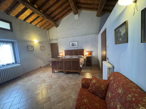 Camera spaziosa all'Agriturismo Aggazzotti con letto in legno, pavimenti in cotto e soffitto con travi rustiche