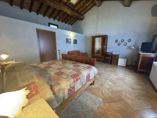Spaziosa camera da letto ad Agriturismo Aggazzotti con travi in legno, letto matrimoniale, TV, armadio e arredo rustico italiano