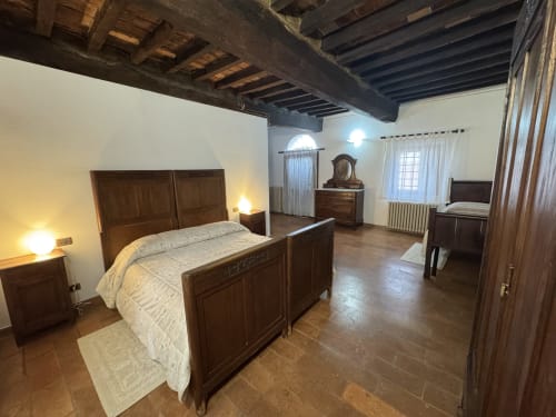 Spacious bedroom at Agriturismo Aggazzotti with wooden beams, dark wood furniture, and terracotta floors