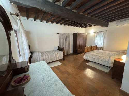 Spacious bedroom at Agriturismo Aggazzotti with wooden beams, three beds, and warm lighting in Colombaro, Italy