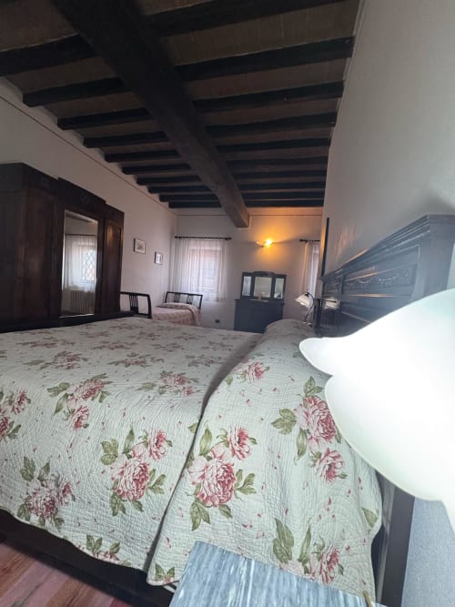 Bedroom at Agriturismo Aggazzotti, Colombaro, featuring floral bedspread, exposed wooden beams, and traditional Italian