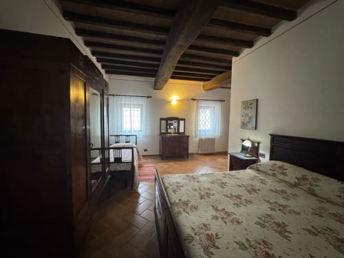 Spacious bedroom at Agriturismo Aggazzotti with rustic beams, floral bedding, dark wood furniture, and windows