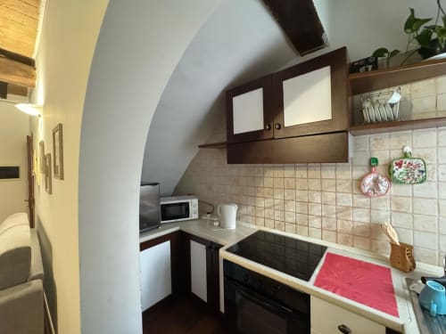 Compact kitchen in Agriturismo Aggazzotti apartment with angled ceiling, dark wood cabinets, beige tiles, and modern