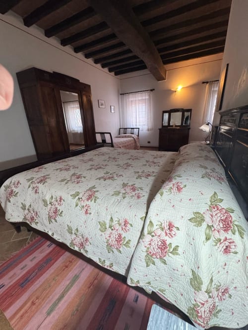 Spacious bedroom at Agriturismo Aggazzotti with two beds, floral quilts, dark wood beams, and rustic charm in Colombaro,