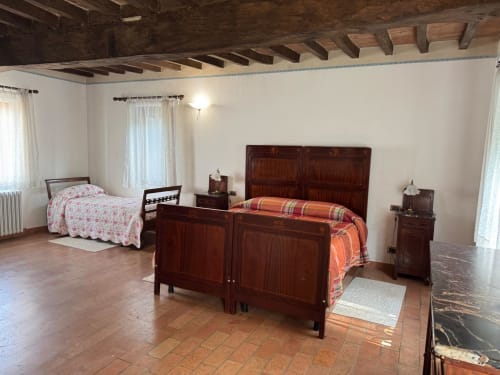 Spacious bedroom at Agriturismo Aggazzotti with exposed wood beams, two wooden beds, and terra cotta flooring