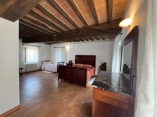 Spacious bedroom at Agriturismo Aggazzotti with exposed wooden beams, dark wood beds, and terracotta floors in Colombaro,