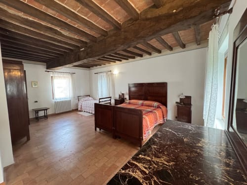 Spacious bedroom at Agriturismo Aggazzotti with wooden beams, dark wood bed, and marble flooring in Colombaro, Italy