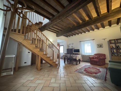 Spacious open-plan living area at Agriturismo Aggazzotti with wooden beams, spiral staircase, and furnished seating in