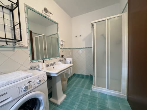 Modern bathroom with green tiled floor, sink, shower, and washing machine at Agriturismo Aggazzotti