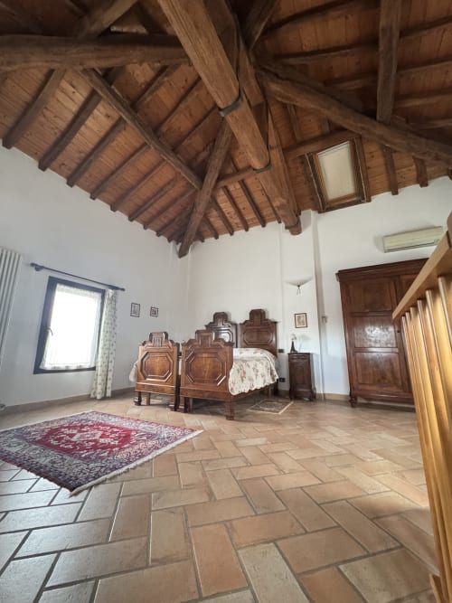 Spacious bedroom at Agriturismo Aggazzotti with ornate wooden bed, terracotta floors, and exposed timber ceiling beams,