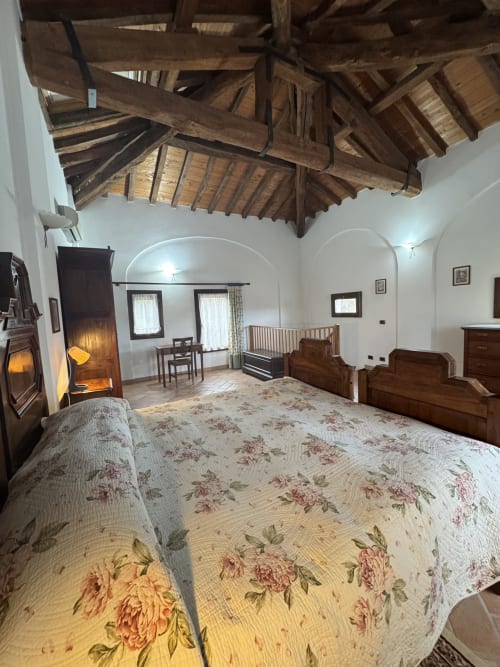Spacious bedroom at Agriturismo Aggazzotti with rustic wooden beams, fireplace, and floral bedding