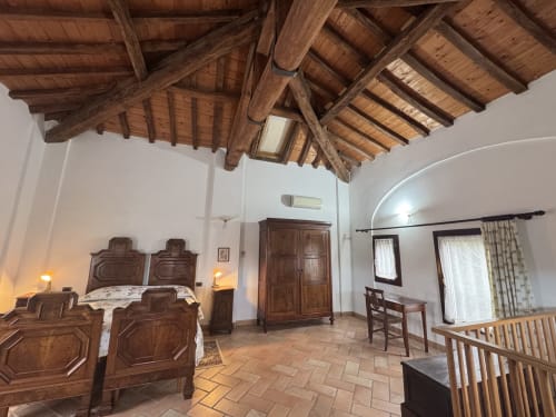 Spacious bedroom with wooden beamed ceiling, two beds with carved headboards, and terracotta floors at Agriturismo