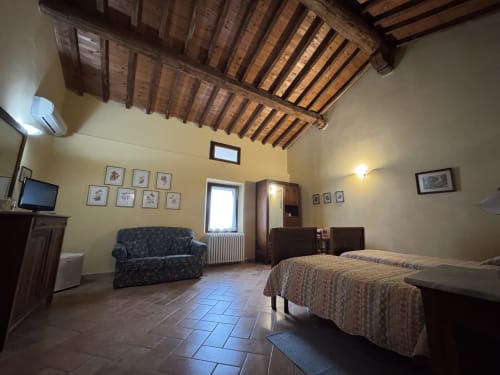 Ampia camera all'Agriturismo Aggazzotti con soffitto in travi di legno, letto, divano e pavimento in cotto a Colombaro