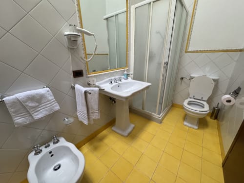 Bagno della Camera 7 in Agriturismo Aggazzotti: piastrelle bianche, pavimento giallo, lavabo su colonna e box doccia