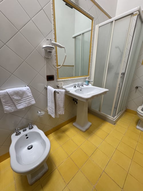Bagno dell'Agriturismo Aggazzotti con pavimento in piastrelle gialle, lavabo su colonna, bidet e box doccia