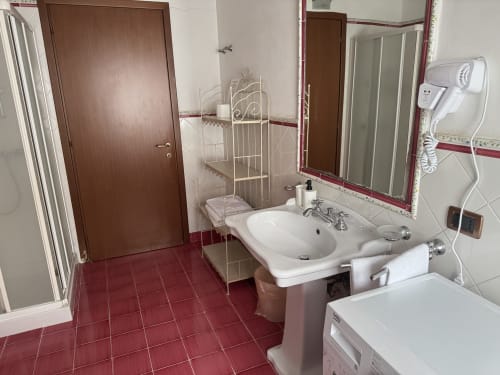 Bathroom with red tile floor, white sink, mirror, brown door, and shower at Agriturismo Aggazzotti in Colombaro, Italy