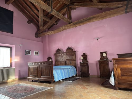Spacious bedroom at Agriturismo Aggazzotti with pink walls, wooden beams, and antique furniture in Colombaro, Italy