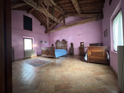 Spacious bedroom with pink walls, wooden beams, terracotta floors, and antique furniture at Agriturismo Aggazzotti, Colombaro