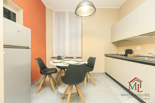 Zona cucina-pranzo moderna nell'appartamento ML White House Genova con parete accent arancione, tavolo rotondo e sedie nere