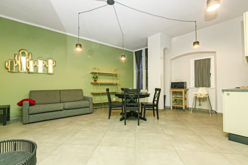 Zona living dell'appartamento a Genova con parete verde salvia, divano grigio, tavolo da pranzo e illuminazione a sospensione