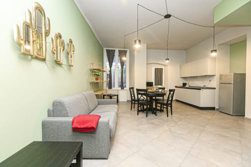 Moderno appartamento open-plan a Genova con divano grigio, tavolo da pranzo, cucina e decorazione neon cactus
