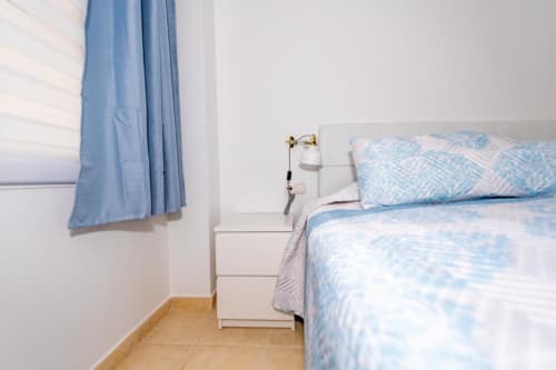 Dormitorio luminoso en Smart Rent Fuerteventura con ropa de cama azul estampada, mesilla blanca y acceso a balcón