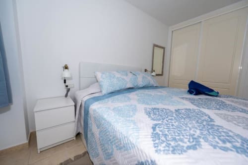 Dormitorio luminoso con ropa de cama azul y blanca, mesita blanca y armario empotrado en apartamento Casa Laguna de Smart Rent