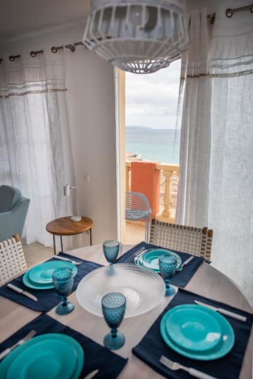 Comedor de Casa Laguna con puestos de mesa turquesas, con vistas a la playa de Fuerteventura y al océano desde el balcón