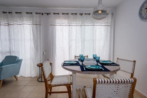 Comedor Casa Laguna con mesa redonda, sillas de madera, vajilla turquesa y cortinas blancas translúcidas en Smart Rent