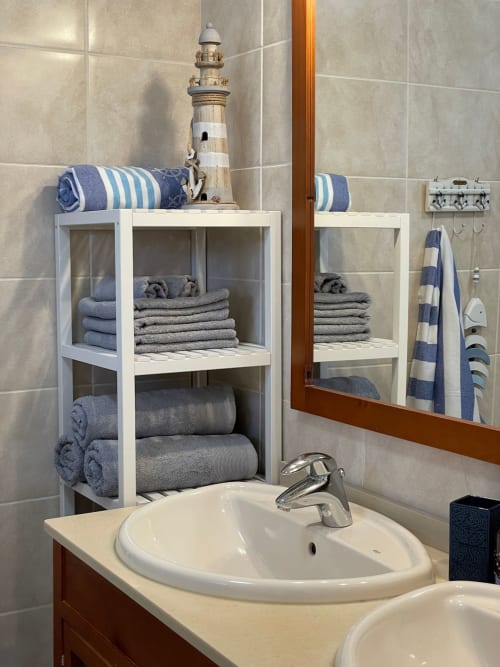 Baño de estilo náutico en Smart Rent Fuerteventura con estanterías blancas, toallas rayadas y decoración con faro.