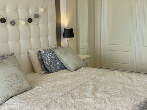 Dormitorio moderno en Smart Rent Fuerteventura con cabecero acolchado blanco, ropa de cama estampada, almohadas decorativas y negro