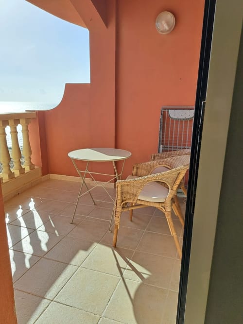 Soleada terraza con muros de terracota, sillas de mimbre, mesa redonda y vistas al océano desde área privada