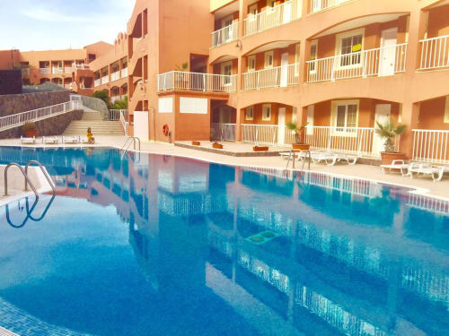 Piscina del resort con edificios de terracota, barandillas blancas y tumbonas en Smart Rent Fuerteventura