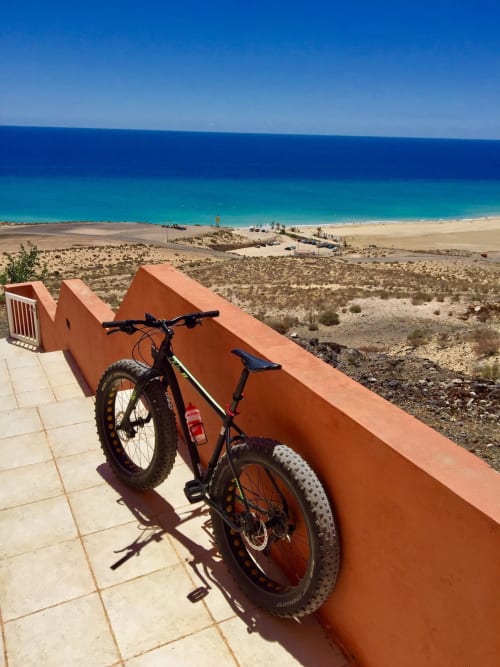 Bicicleta de montaña apoyada en pared naranja con vista a playa turquesa en propiedad costera de Fuerteventura