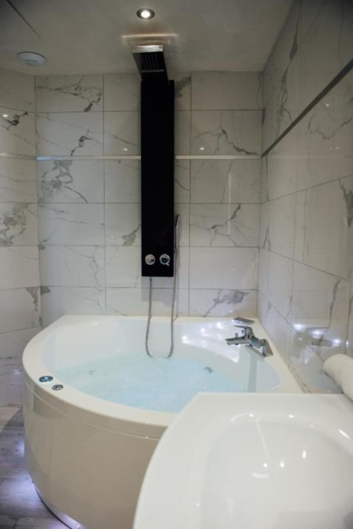 Baignoire de luxe avec douche pluie encastrée dans une salle de bains carrelée de marbre à l'Hôtel Amirauté La Baule