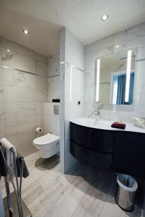 Modern bathroom in Hôtel Amirauté La Baule with marble tiles, illuminated mirror, black vanity, and shower area