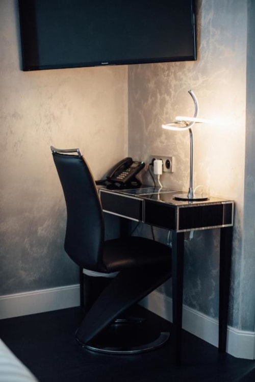 Modern office nook at Hôtel Amirauté La Baule with sleek black desk, chair, desk lamp, and wall-mounted TV in contemporary
