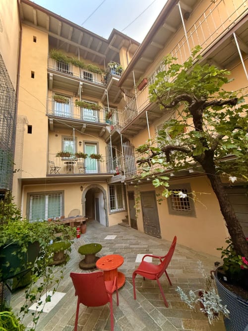 Charmanter Innenhof der Borgovivobg Apartments in Bergamo mit roten Stühlen, efeubedeckten Wänden und gelbem Gebäude