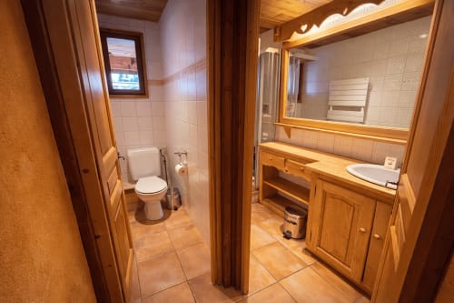 Salle de bain spacieuse chez Francine avec meuble-vasque en bois, miroir, toilettes et murs carrelés à Notre Dame de Bellecombe