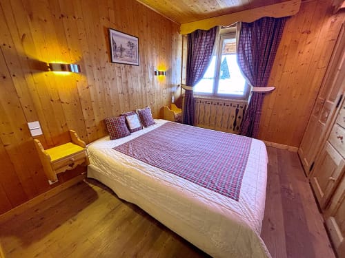Chambre chaleureuse lambrisée à Chez Francine avec lit queen-size, linge de lit à carreaux violets, vue montagne et éclairage chaleureux