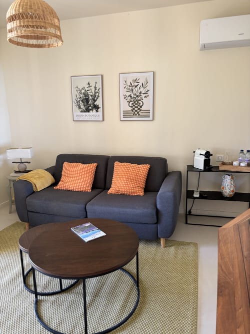 Salon moderne avec canapé bleu marine, coussins orange et table ronde en bois au Mas des Vignes à Rochegude