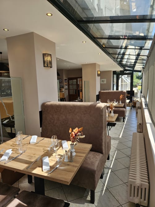 Salle à manger contemporaine de l'hôtel La Route d'Argent à Bozouls avec banquettes marron, tables en bois et verrière.