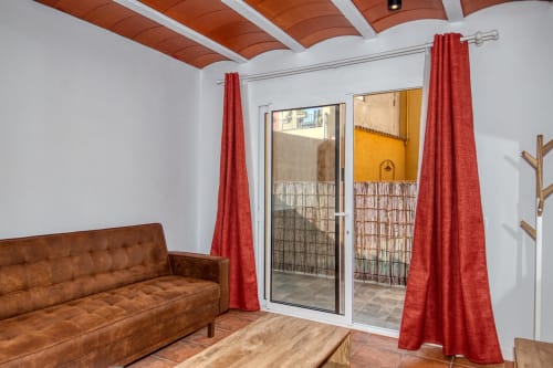 Bright living room at Finques Garcia Enrich, Palafrugell, with brown leather sofa, red curtains, and terrace access doors