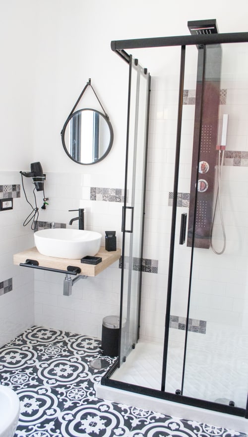 Bagno moderno presso LH51 Napoli con specchio rotondo, lavabo da appoggio, box doccia con telaio nero e pavimento con piastrelle geometriche