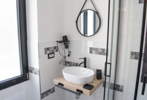 Modern bathroom sink with round white basin at LH51 Rooms in Naples, featuring black fixtures and mirror
