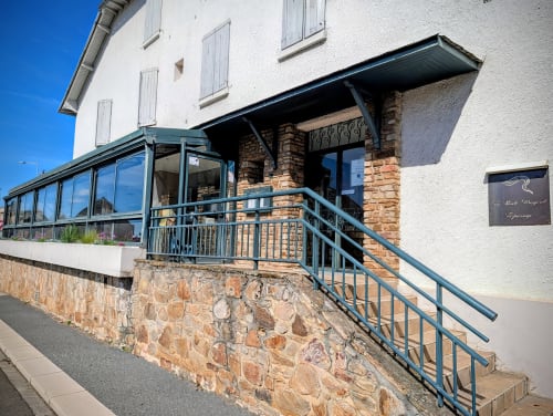 Entrée de l'Hôtel La Route d'Argent avec façade en pierre, véranda vitrée et balustrades métalliques à Bozouls, France