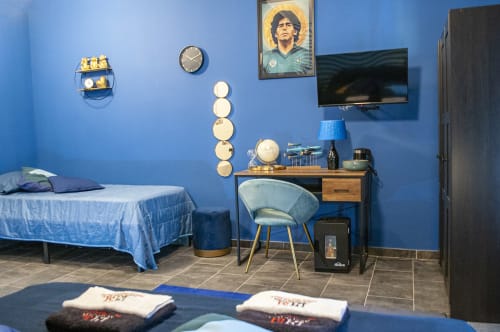 Camera azzurra brillante alle LH51 Rooms di Napoli con letto, scrivania, TV e poster di Maradona